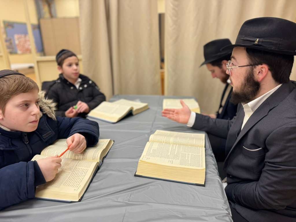 A yeshiva student learning with two boys over an open religious text
